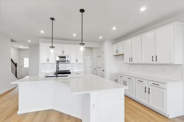 a kitchen with kitchen island a stove a sink a refrigerator and white cabinets with wooden floor