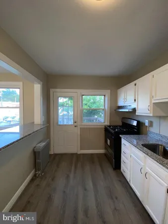 a kitchen with granite countertop a stove a sink wooden floor and cabinets