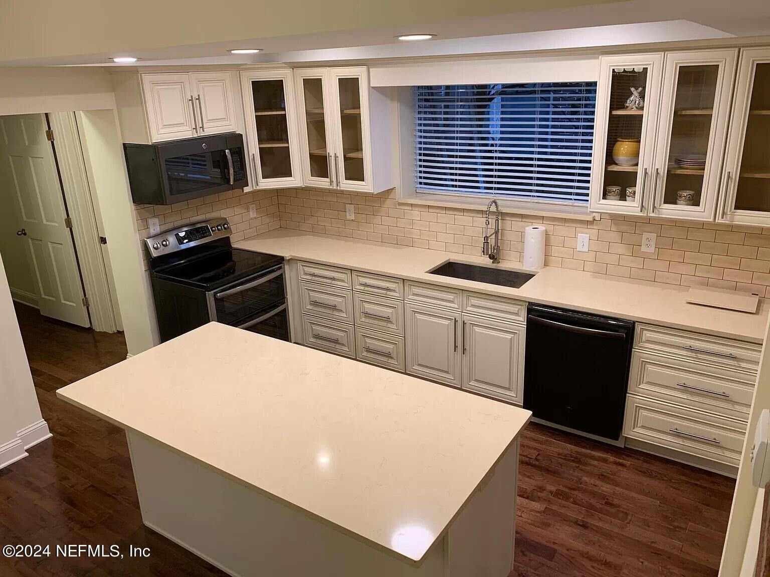 a kitchen with stainless steel appliances a stove a sink a microwave a refrigerator white cabinets and wooden floor