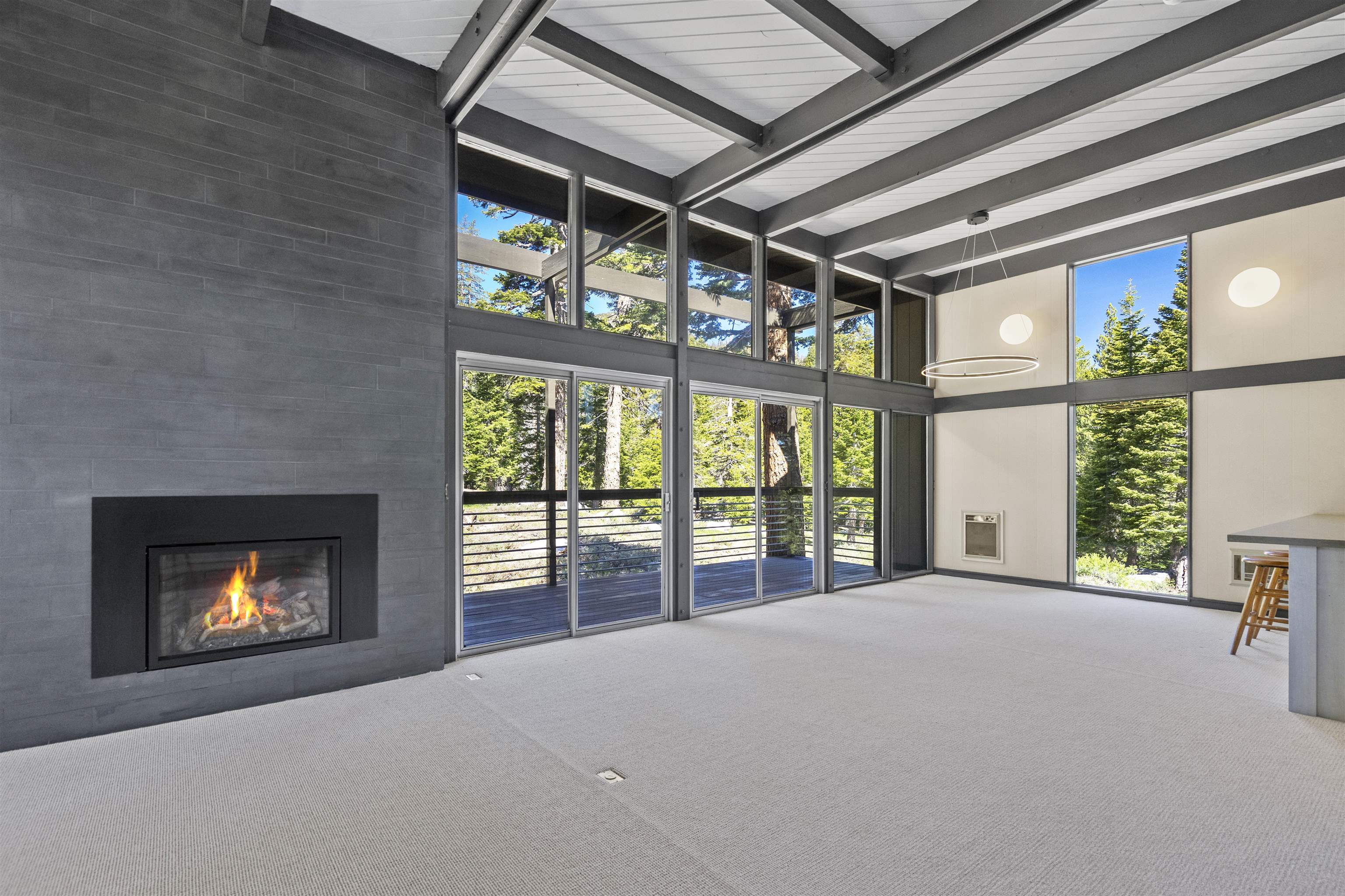 2570 Old Mammoth Road Mammoth Lakes, CA 93546 - Photo 2 of 39 Spacious room featuring a floor-to-ceiling fireplace with dark-toned tile surround, expansive windows, exposed beam ceiling, light-toned carpeting, and sliding glass doors opening to an exterior deck