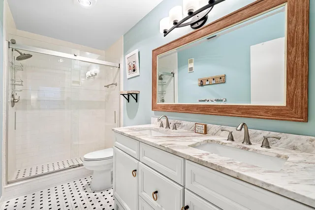 a bathroom with a granite countertop sink a toilet a mirror a vanity and shower