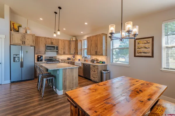 a open kitchen with stainless steel appliances granite countertop a refrigerator a stove top oven a sink dishwasher a dining table and chairs with wooden floor