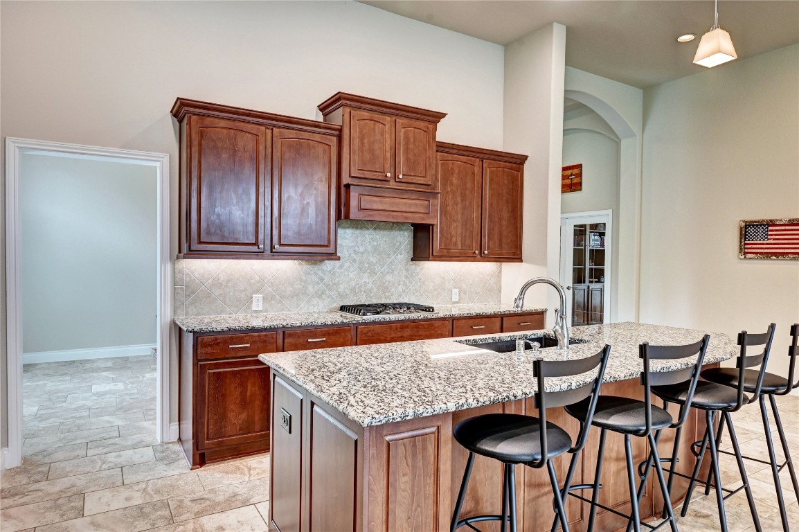 335 Fox Trail Road Montgomery, TX 77316 - Photo 12 of 47 This kitchen features elegant dark wood cabinetry, a large granite island with seating, and a modern faucet. The space is accented by a tile backsplash and light flooring, creating a warm and inviting atmosphere.