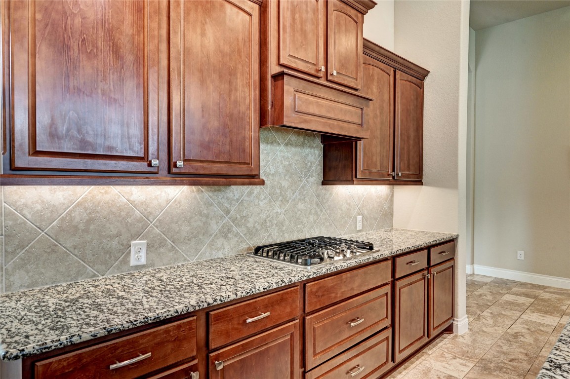 335 Fox Trail Road Montgomery, TX 77316 - Photo 13 of 47 This kitchen features elegant wooden cabinets, a granite countertop, a modern gas stovetop, and a neutral tile backsplash, creating a warm and inviting cooking space.
