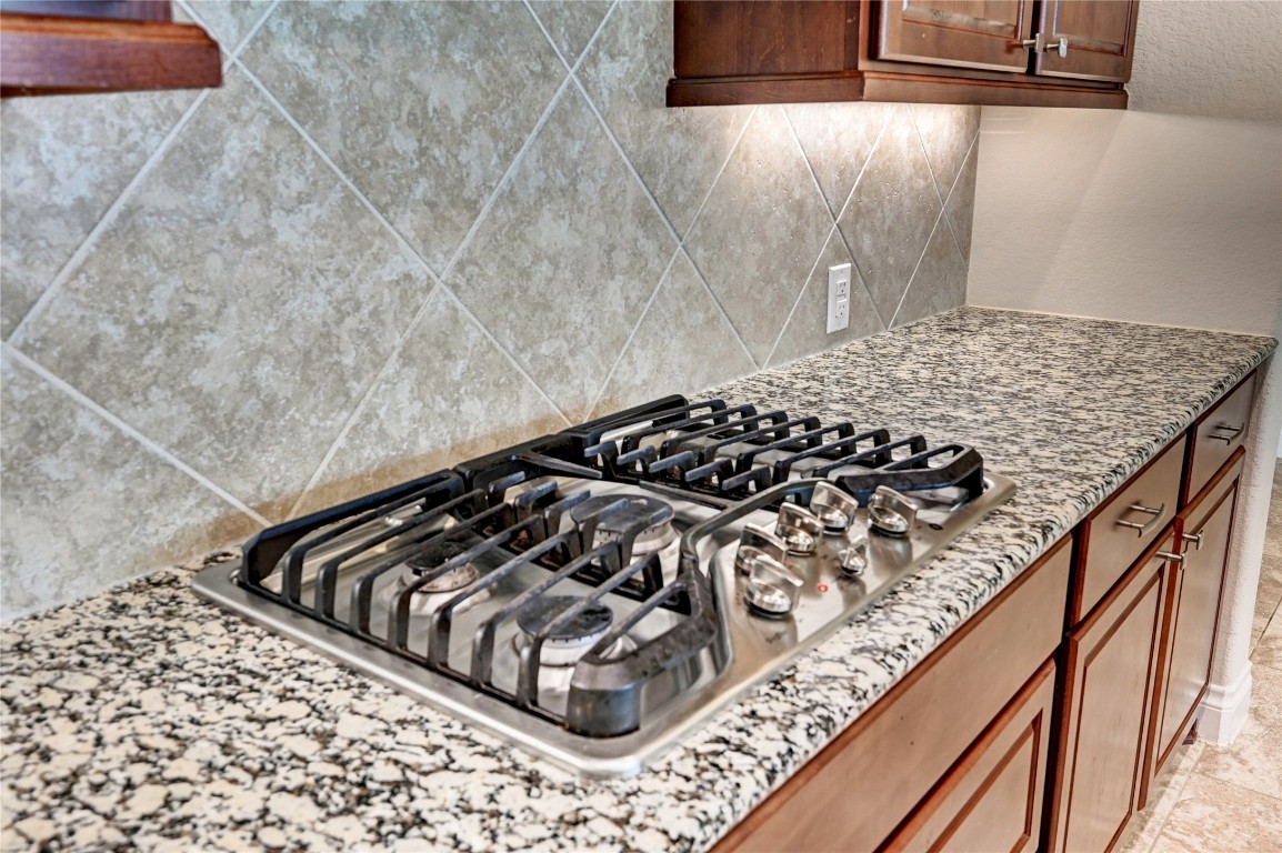 335 Fox Trail Road Montgomery, TX 77316 - Photo 14 of 47 This kitchen features a sleek gas cooktop set in granite countertops with a diamond-patterned tile backsplash and rich wood cabinetry, offering a stylish and functional cooking space.