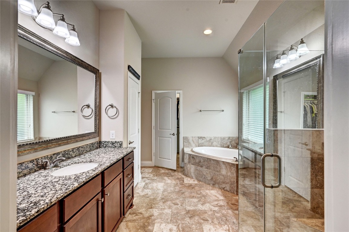 335 Fox Trail Road Montgomery, TX 77316 - Photo 17 of 47 This primary bathroom features a spacious layout with a granite-topped double vanity, large framed mirrors, a glass-enclosed shower, and a separate soaking tub. The neutral tile flooring and abundant natural light create a serene atmosphere.