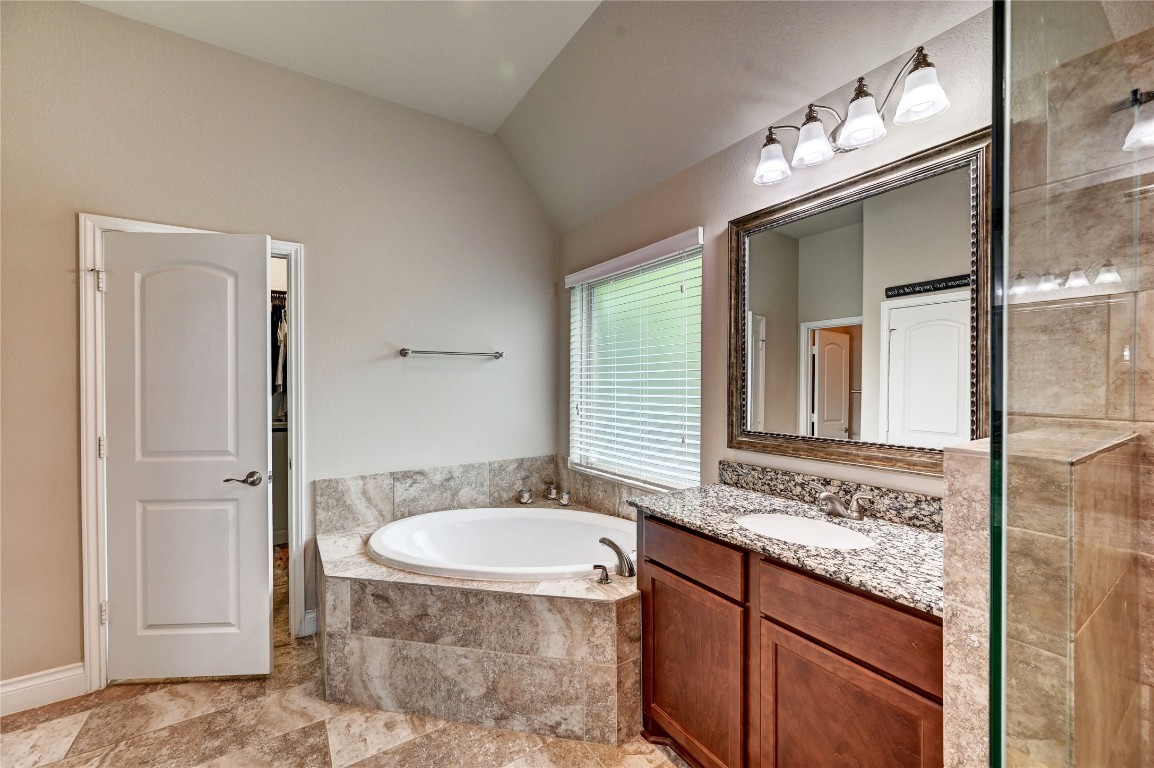 335 Fox Trail Road Montgomery, TX 77316 - Photo 18 of 47 This primary bathroom features a luxurious corner bathtub with tile surround, a granite countertop with a large mirror, and ample cabinet storage. Natural light streams in through a window with blinds, and there’s a separate shower area for convenience.