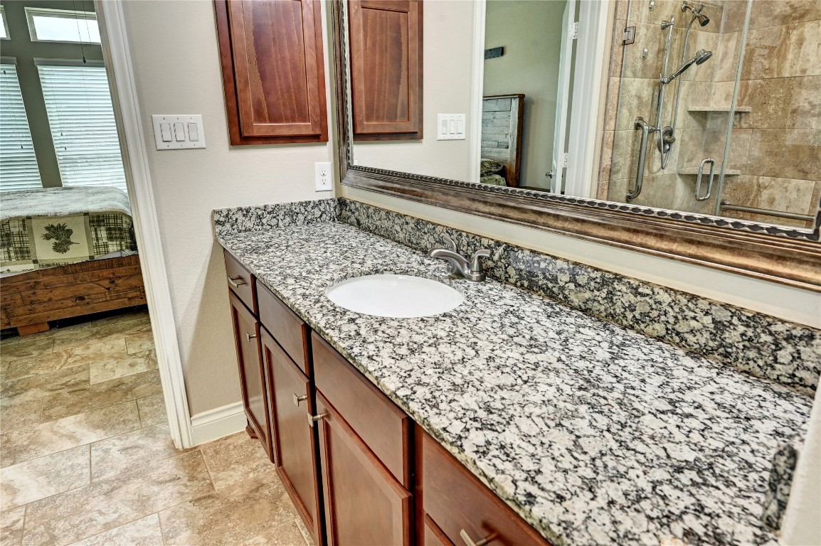 335 Fox Trail Road Montgomery, TX 77316 - Photo 20 of 47 This primary bathroom features a granite countertop, wooden cabinetry, and a large mirror. The adjoining room has a tiled shower with glass doors and a glimpse of a cozy bedroom with natural light.