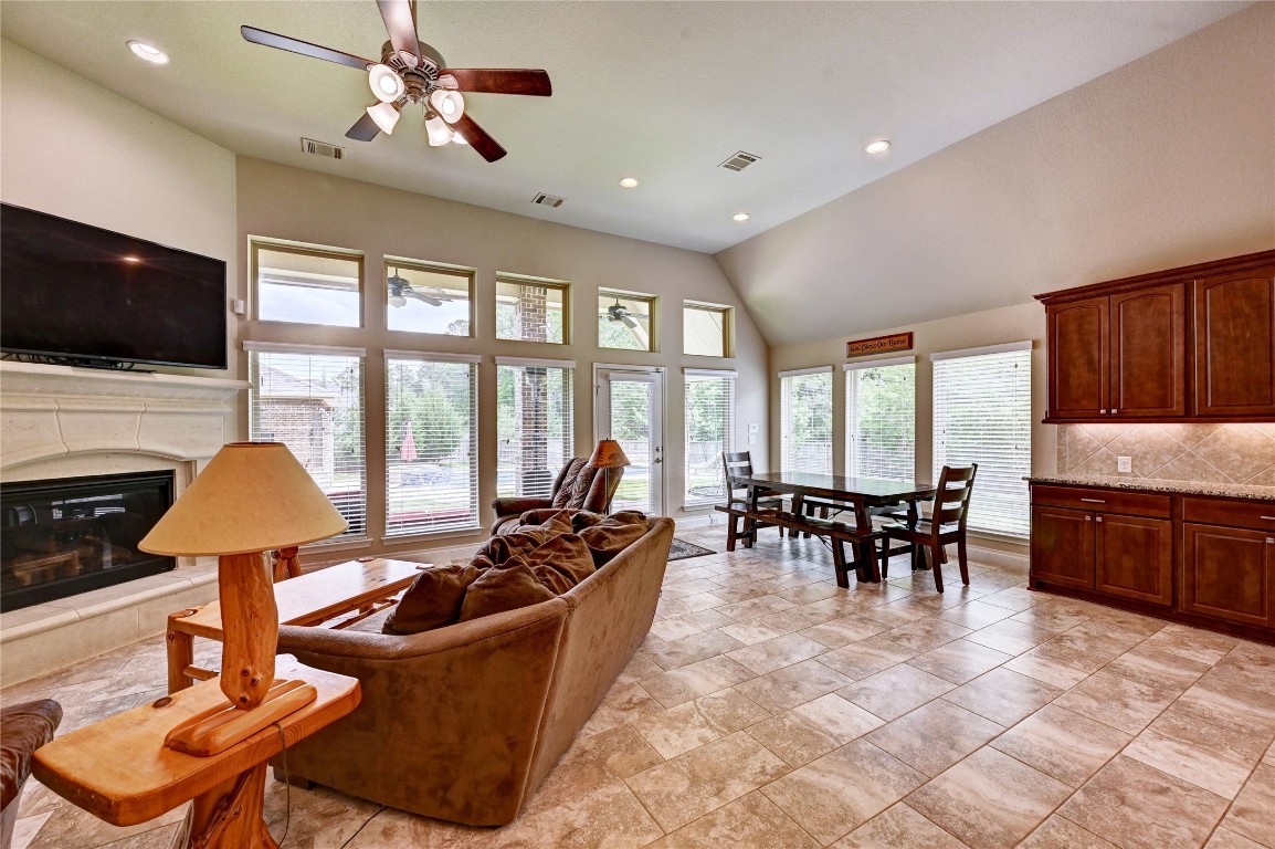335 Fox Trail Road Montgomery, TX 77316 - Photo 22 of 47 This spacious living area features high ceilings and abundant natural light from large windows. It includes a cozy fireplace, tile flooring, and an open layout with a dining area. The room is complemented by warm wood cabinetry and modern lighting fixtures.