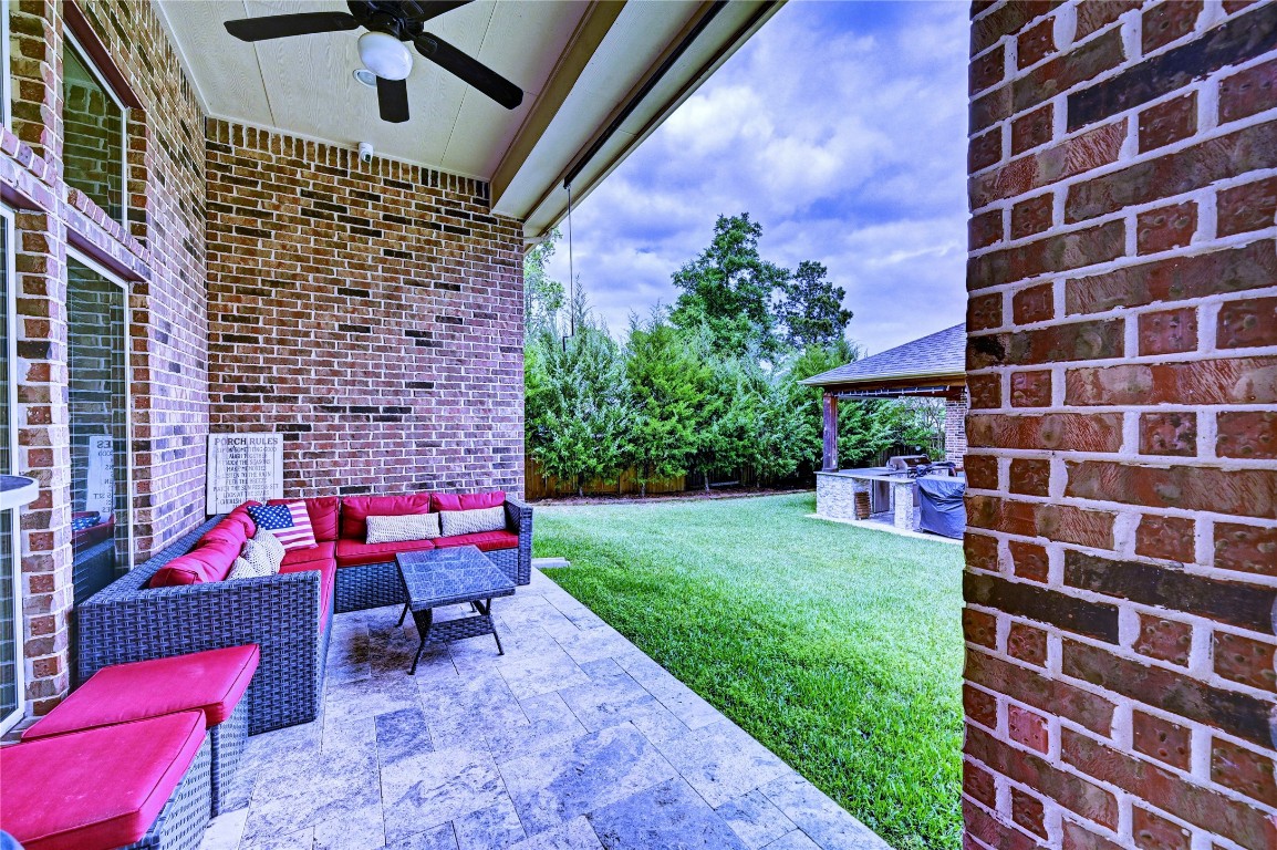 335 Fox Trail Road Montgomery, TX 77316 - Photo 24 of 47 This photo showcases a cozy outdoor patio area with brick walls, a ceiling fan, and comfortable seating. The space opens up to a lush green lawn, with a view of a covered outdoor kitchen or grill area, making it perfect for entertaining.