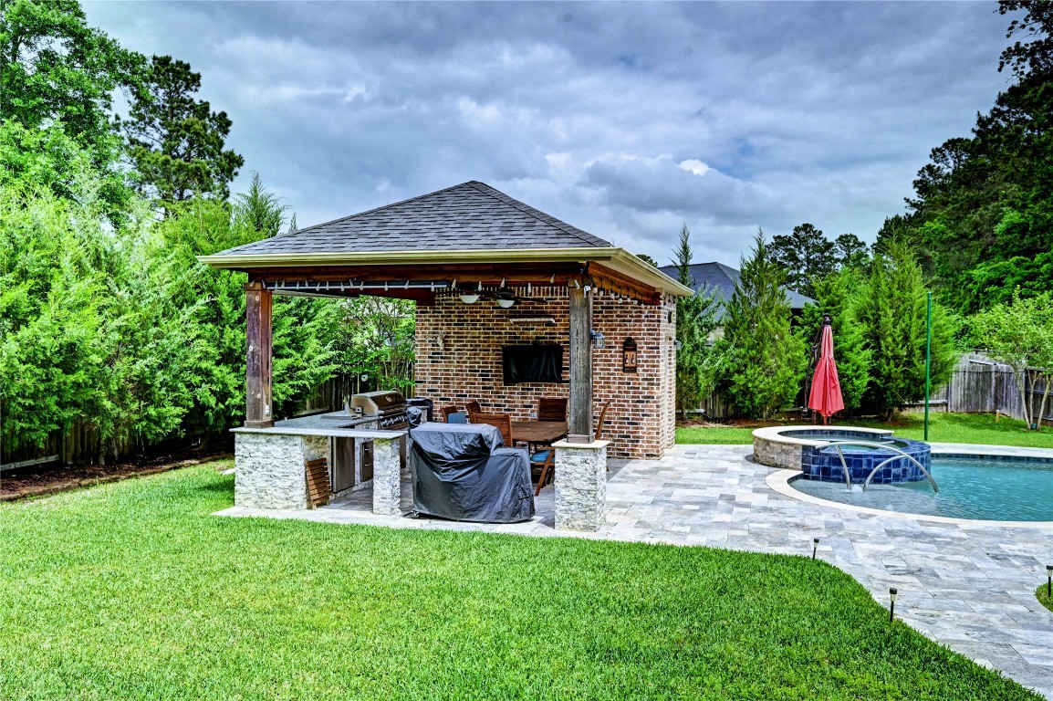 335 Fox Trail Road Montgomery, TX 77316 - Photo 25 of 47 This backyard features a cozy covered cabana features an outdoor kitchen, wooden pillars, a seating area, extra storage , a half bath ,perfect for outdoor entertaining. It overlooks a spacious pool with a hot tub, surrounded by lush greenery for privacy.
