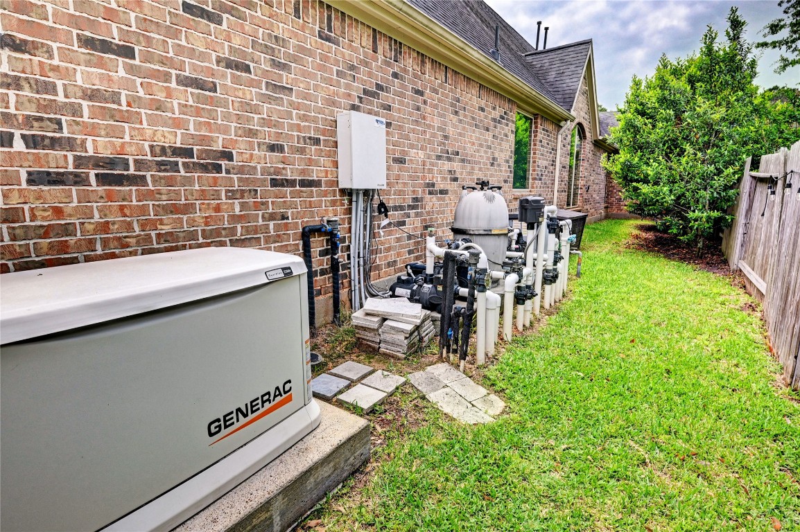 335 Fox Trail Road Montgomery, TX 77316 - Photo 31 of 47 This photo shows the side of a brick house with a well-maintained lawn, featuring a Generac generator and pool equipment. The area is neatly organized, with a wooden fence and some greenery providing privacy.
