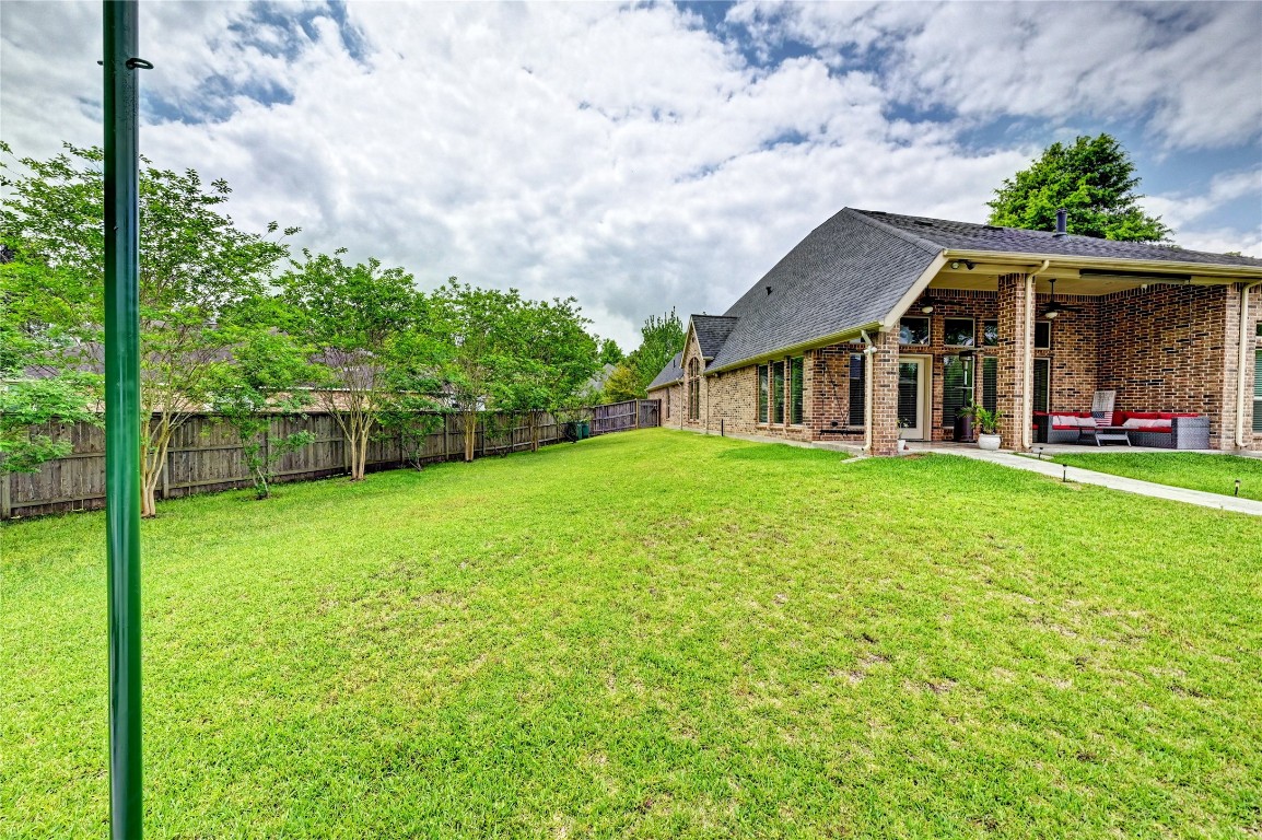 335 Fox Trail Road Montgomery, TX 77316 - Photo 32 of 47 This photo showcases a spacious backyard with a well-maintained lawn, bordered by a wooden fence and trees for privacy. The brick house features a covered patio with outdoor seating, offering a welcoming space for relaxation or entertaining.