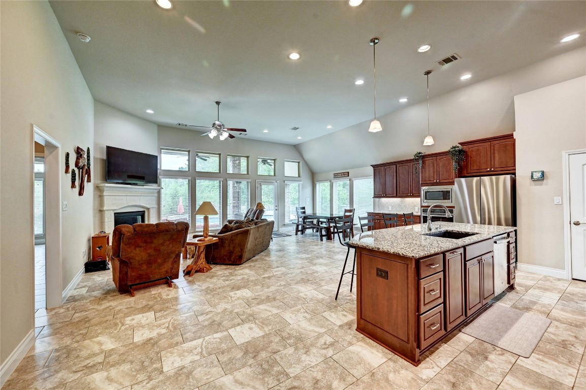 335 Fox Trail Road Montgomery, TX 77316 - Photo 9 of 47 This open-concept living space features a spacious kitchen with a large island, granite countertops, and stainless steel appliances. It seamlessly flows into a cozy living area with a fireplace and abundant natural light from large windows, creating a welcoming and airy atmosphere.