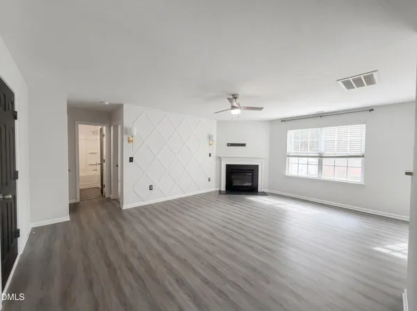 an empty room with wooden floor fireplace and windows
