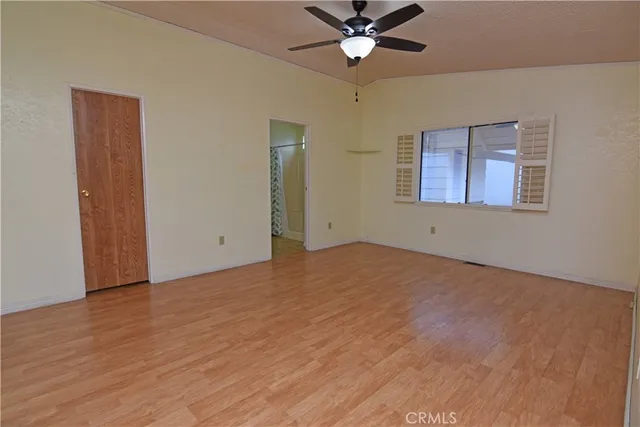 an empty room with wooden floor fan and windows