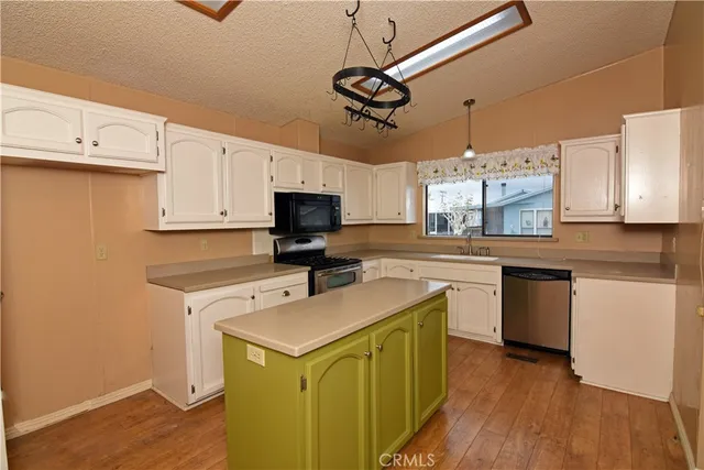 a kitchen with a sink stainless steel appliances white cabinets and wooden floor