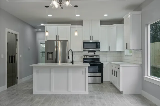 a kitchen with stainless steel appliances kitchen island granite countertop a refrigerator a stove a sink and white cabinets with wooden floor