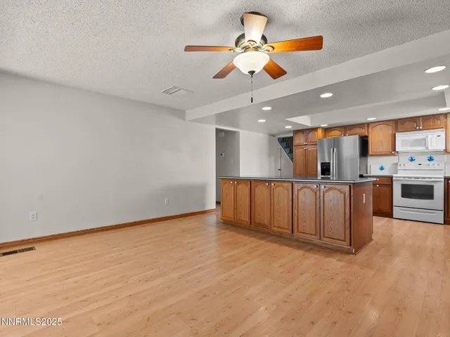 a view of an empty room with a kitchen and chandelier fan