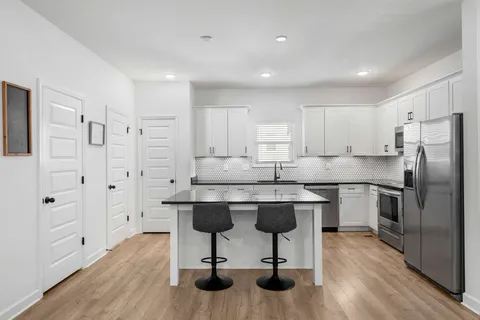a kitchen with stainless steel appliances granite countertop a refrigerator a sink dishwasher a stove and white cabinets with wooden floor