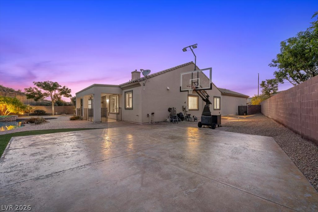 2125 De Rouge Avenue Henderson, NV 89044 - Photo 18 of 96 An inviting backyard oasis features a paved patio, lush landscaping, and a sparkling pool, perfect for twilight entertaining.