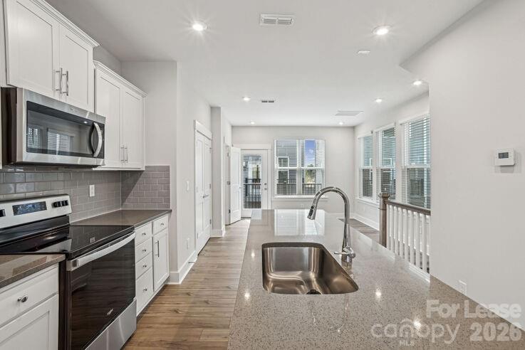 4375 Raleigh Street, Unit C1 Charlotte, NC 28213 - Photo 7 of 19 a kitchen with stainless steel appliances granite countertop a stove top oven a sink a dining table and chairs with wooden floor