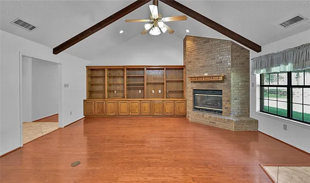 wooden floor in an empty room with a fireplace and a window