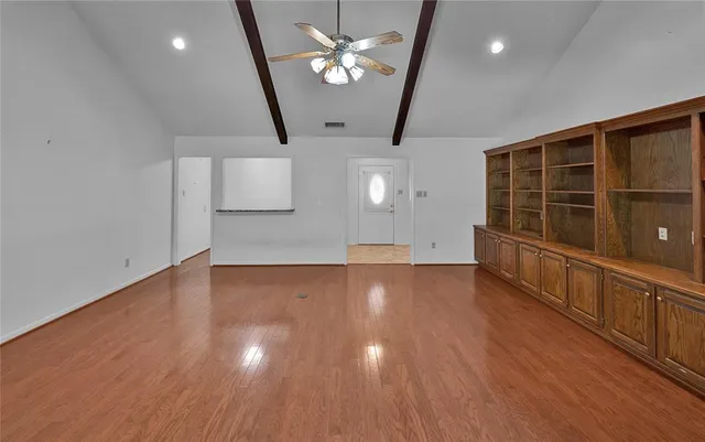 a view of an empty room with wooden floor and a ceiling fan