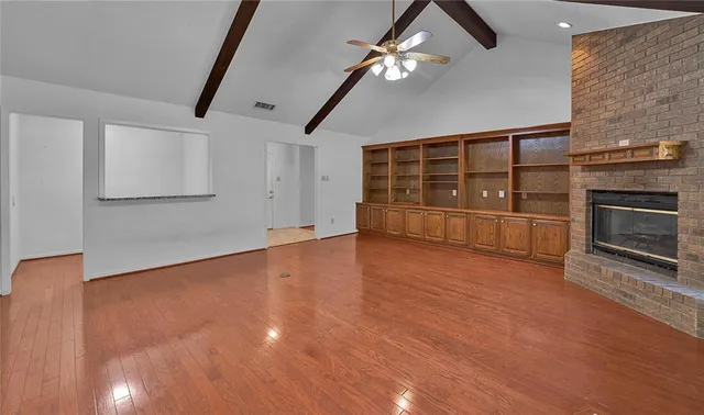 an empty room with wooden floor fireplace and windows