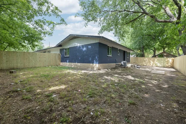 a view of a house with brick walls and a yard with plants and large tree