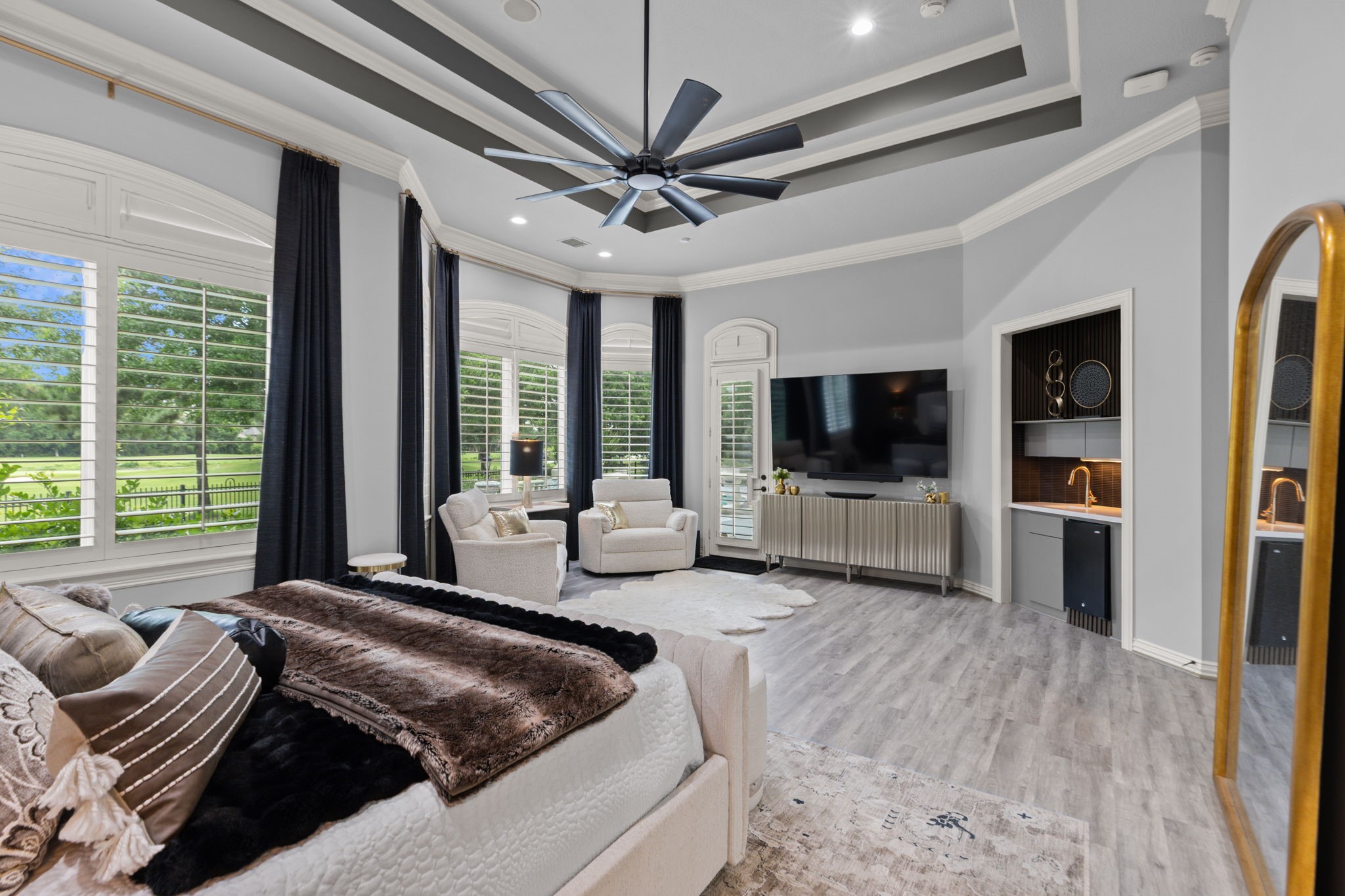 39 Maymont Way Spring, TX 77382 - Photo 21 of 50 Spacious and elegant bedroom with abundant natural light from large windows, featuring a stylish ceiling fan, cozy seating area, and a modern entertainment setup. The room includes a wet bar and has a sophisticated color scheme with luxurious furnishings.