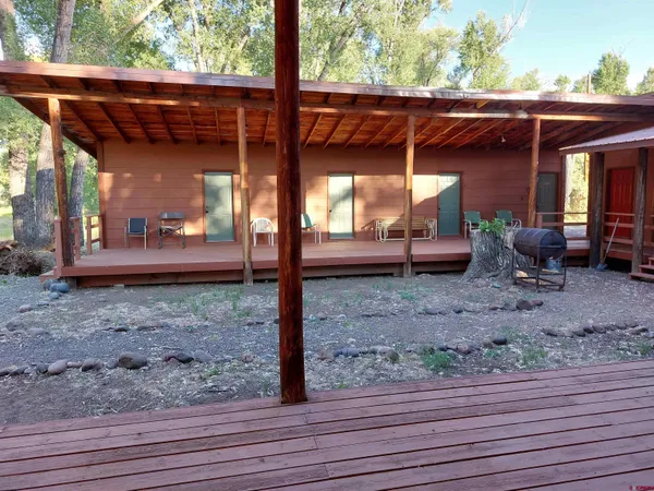 a view of a patio with table and chairs under wooden roof with a barbeque