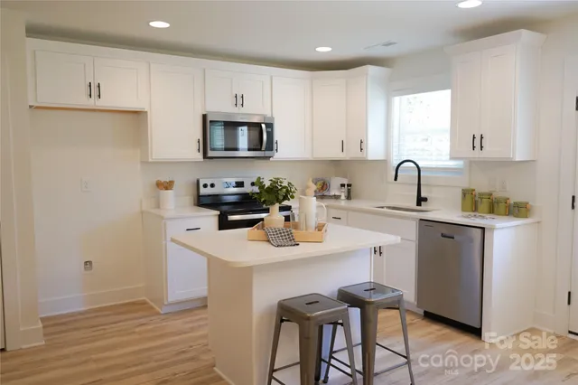 a kitchen with stainless steel appliances a sink a stove a refrigerator cabinets and a dining table with wooden floor