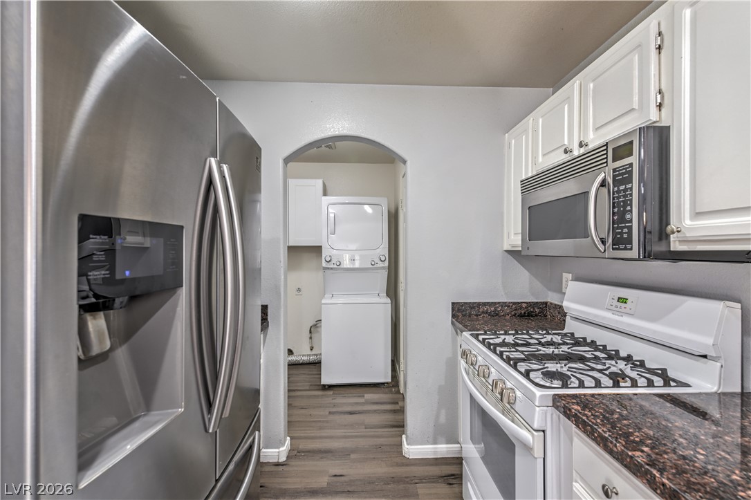 3950 South Sandhill Road, Unit 112 Las Vegas, NV 89121 - Photo 11 of 33 Kitchen with stainless steel appliances, dark wood finished floors, arched walkways, stacked washer / dryer, and white cabinets