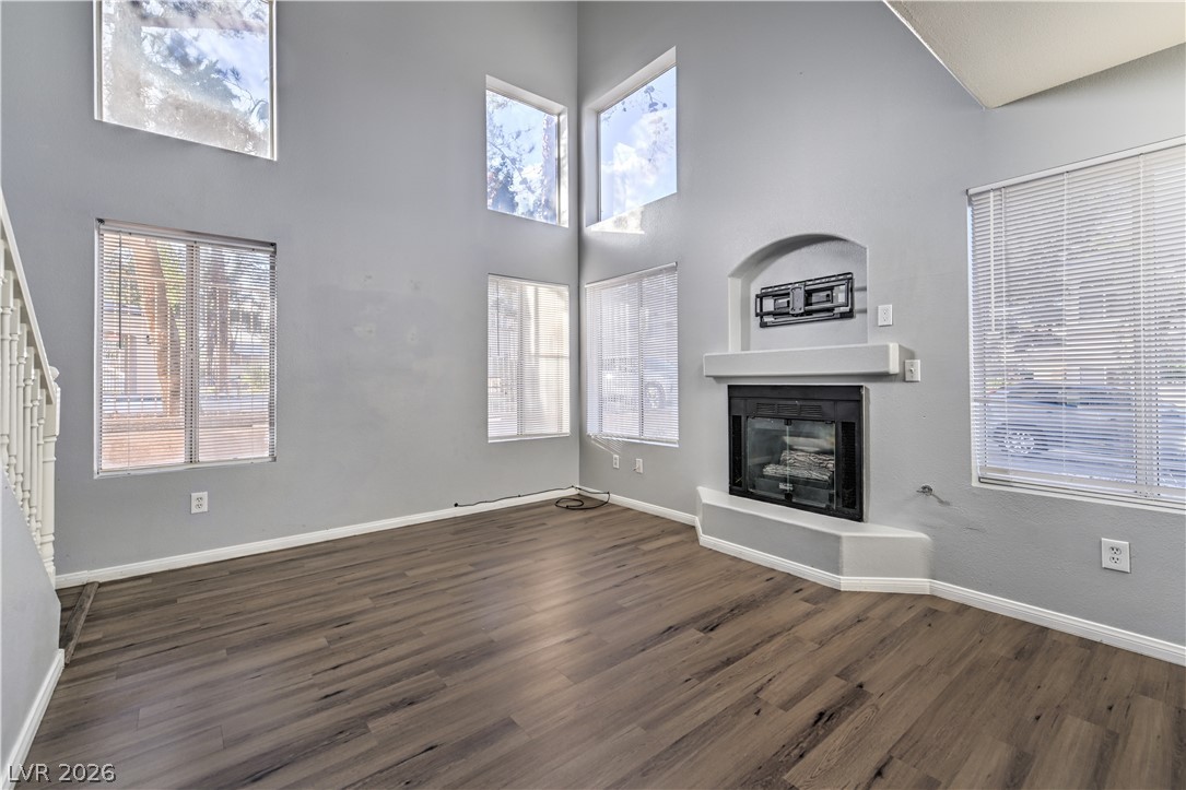 3950 South Sandhill Road, Unit 112 Las Vegas, NV 89121 - Photo 2 of 33 Unfurnished living room featuring baseboards, a towering ceiling, stairway, dark wood-type flooring, and a glass covered fireplace