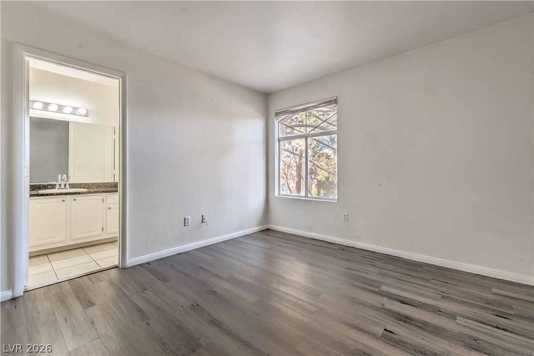 3950 South Sandhill Road, Unit 112 Las Vegas, NV 89121 - Photo 21 of 33 Unfurnished bedroom with ensuite bathroom, baseboards, wood finished floors, and a sink