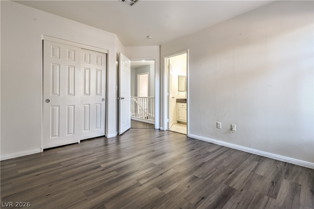 3950 South Sandhill Road, Unit 112 Las Vegas, NV 89121 - Photo 22 of 33 Unfurnished bedroom with a closet, ensuite bathroom, baseboards, visible vents, and dark wood-type flooring