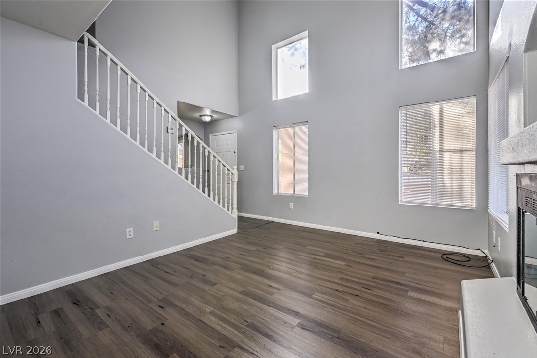 3950 South Sandhill Road, Unit 112 Las Vegas, NV 89121 - Photo 3 of 33 Unfurnished living room featuring stairs, wood finished floors, a fireplace with raised hearth, baseboards, and a towering ceiling