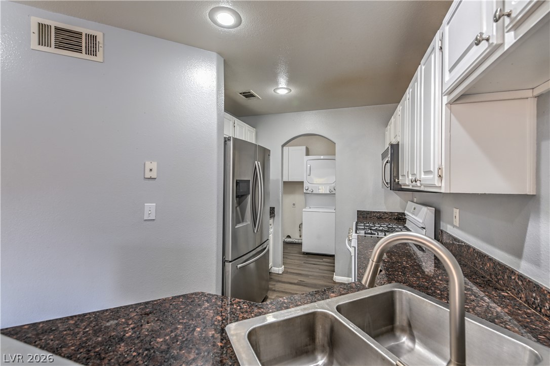 3950 South Sandhill Road, Unit 112 Las Vegas, NV 89121 - Photo 9 of 33 Kitchen featuring white cabinetry, stacked washer / drying machine, stainless steel appliances, a sink, and visible vents