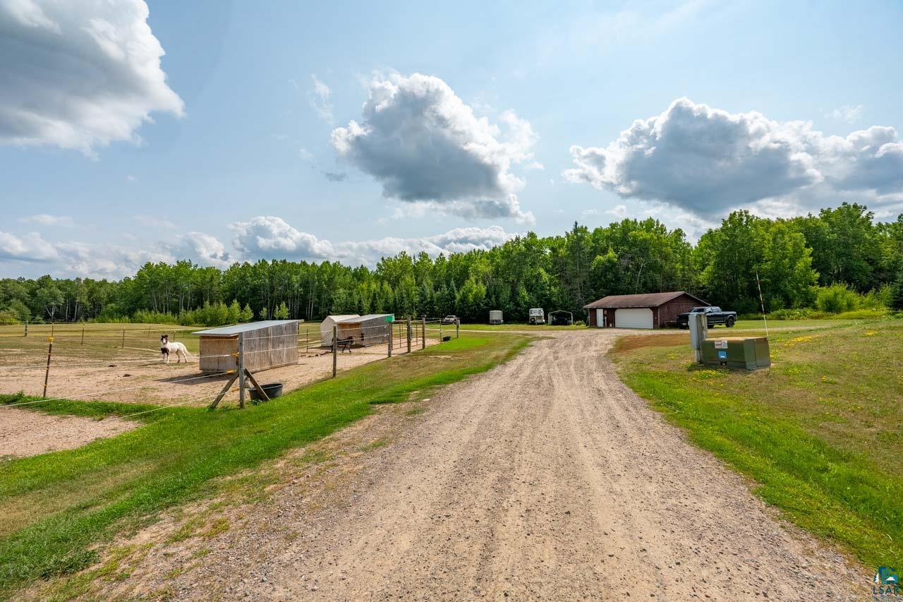 3201 Wilderness Road Makinen, MN 55763 - Photo 44 of 52 Spacious property featuring a gravel driveway, a brown-sided garage building, and a fenced animal enclosure with shelters
