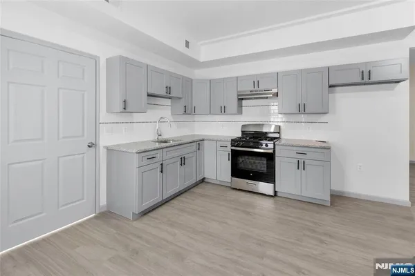 a kitchen with stainless steel appliances granite countertop a stove top oven a sink and white cabinets