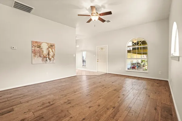 an empty room with wooden floor chandelier fan and windows