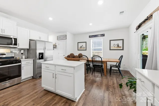 a open kitchen with stainless steel appliances granite countertop a dining table chairs stove refrigerator and cabinets