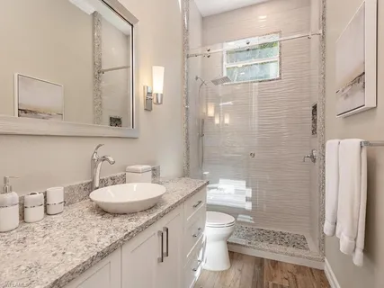 a bathroom with a granite countertop sink a toilet a mirror and shower