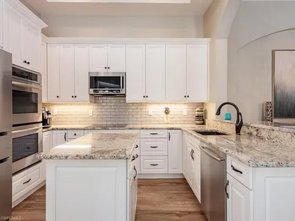 a kitchen with granite countertop a sink stainless steel appliances and white cabinets