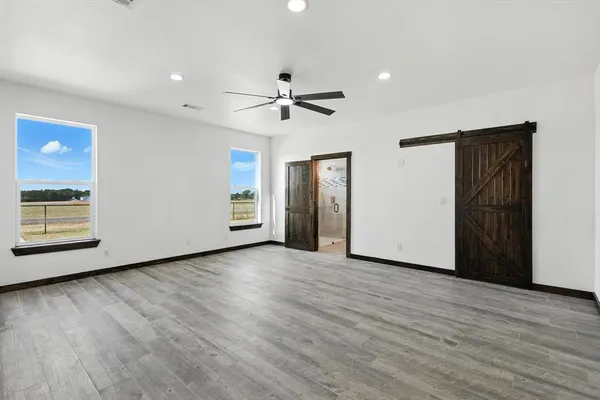 an empty room with wooden floor chandelier fan and windows