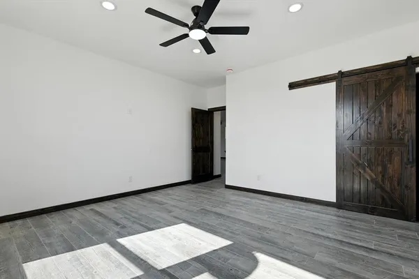 a view of an empty room with wooden floor and a ceiling fan