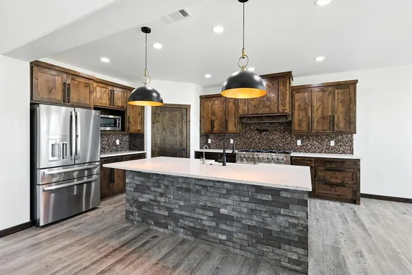 a large kitchen with stainless steel appliances kitchen island granite countertop a refrigerator a oven and a wooden floors