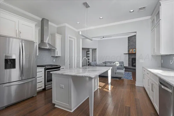 a kitchen with stainless steel appliances granite countertop a stove a refrigerator a sink a stove and white cabinets with wooden floor