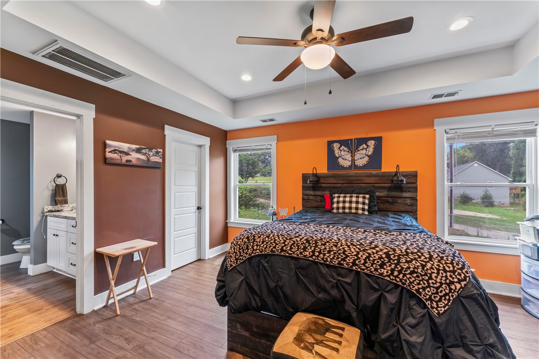 429 Nelson Drive Anderson, SC 29621 - Photo 17 of 32 A well-lit bedroom with a ceiling fan, windows overlooking greenery, and an adjoining bathroom.